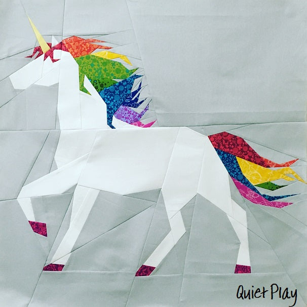unicorn paper pieced patterns sewn in fabrics with a rainbow mane and tail on a grey background
