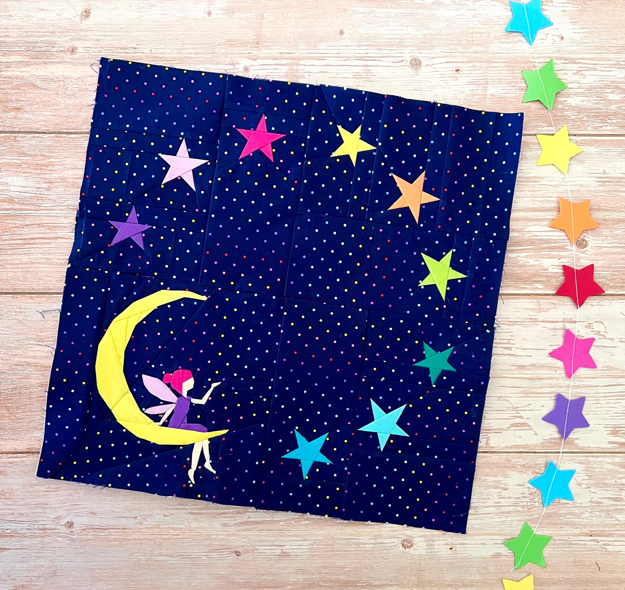 Foundation paper pieced fairy moon quilt block made with colourful star fabrics on a dark night sky background. A magical FPP design ideal for statement quilts and wall hangings.
