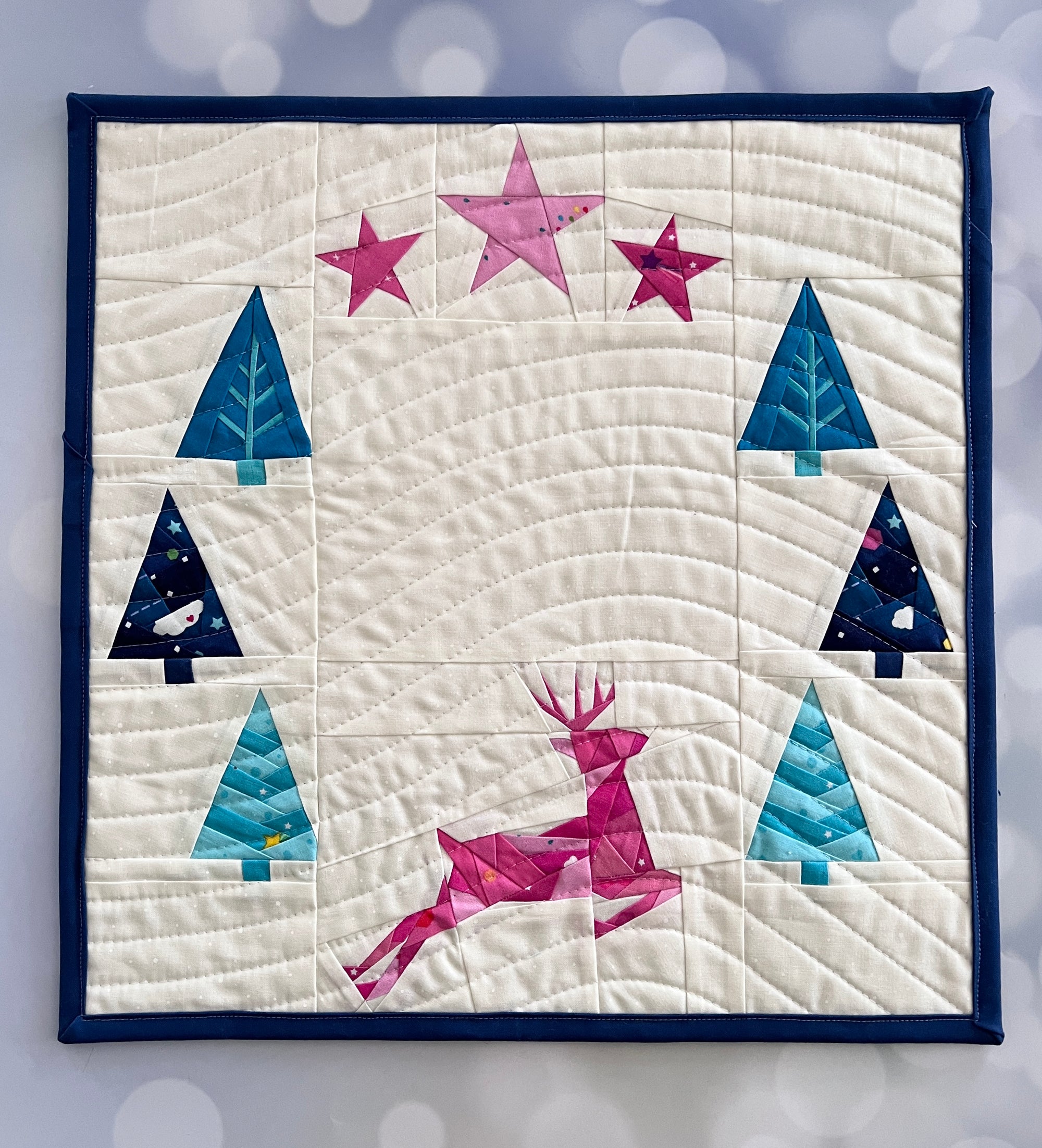 Frolic paper pieced pattern featuring a deer, trees and stars sewn in fabric for a mini quilt in pastel colors