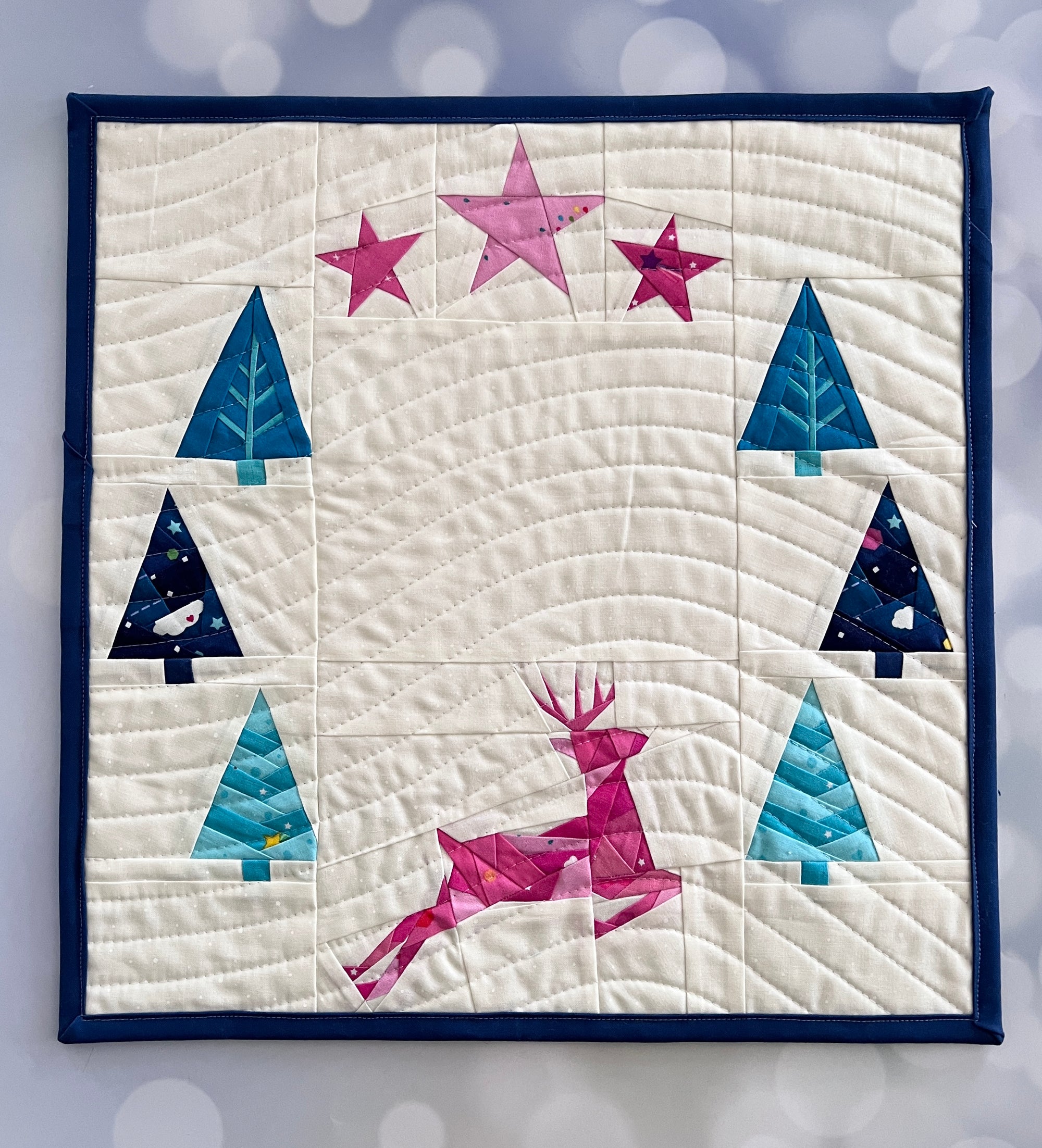 Frolic paper pieced pattern featuring a deer, trees and stars sewn in fabric for a mini quilt