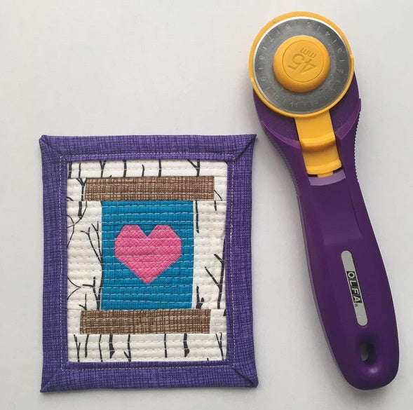 foundation paper pieced mini quilt of a heart on a spool with a rotary cutter