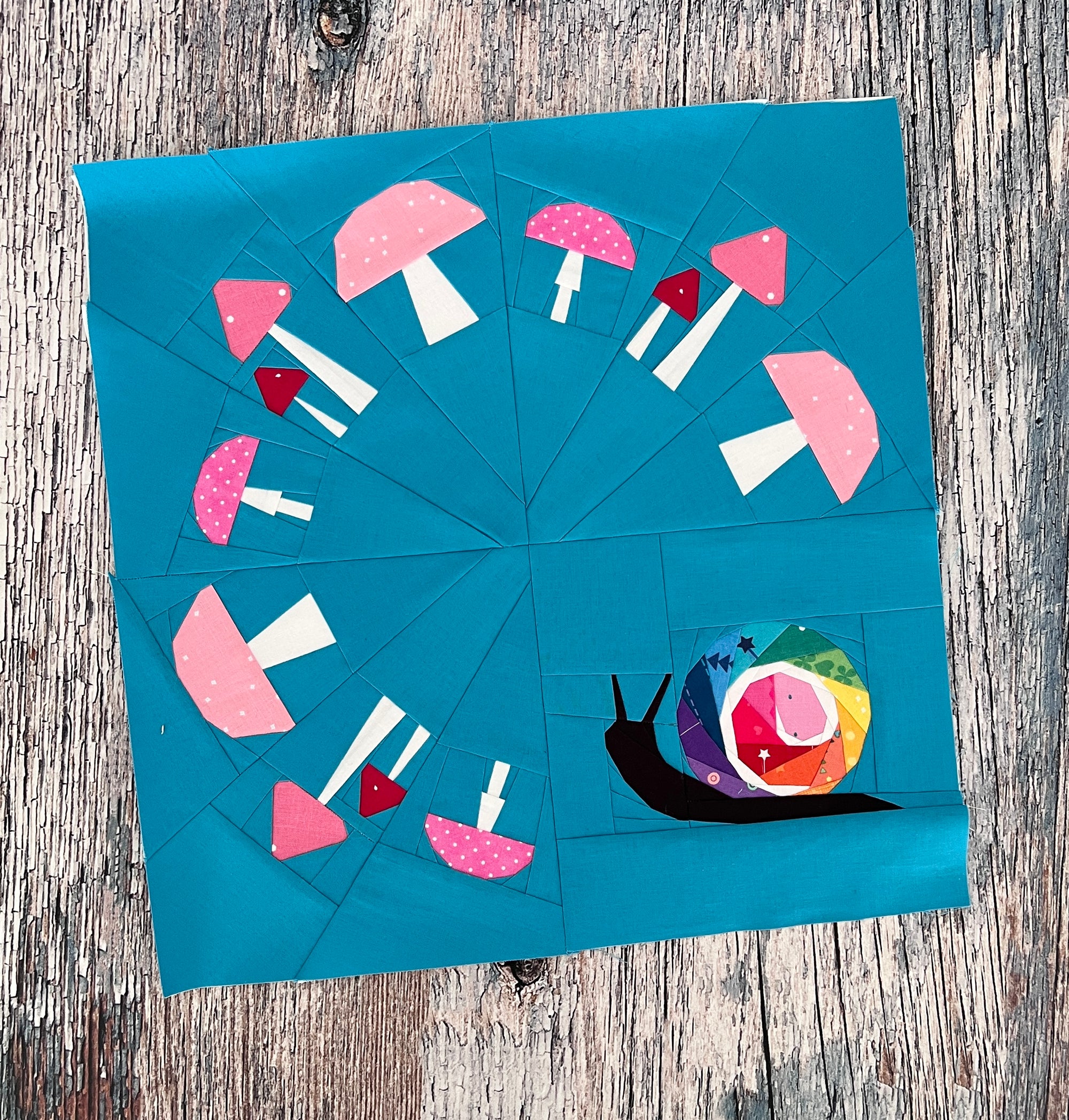 snails pace paper pieced pattern featuring a snail with a ring of mushrooms sewn in fabric with a blue background