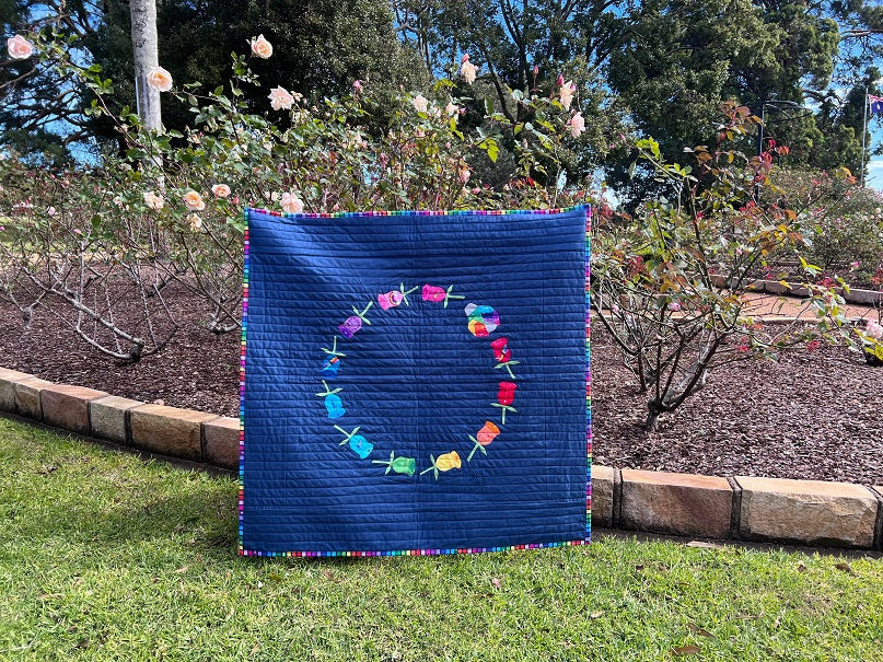 Rosebud quilt paper pieced pattern featuring a ring of roses and a geometric ladybug sewn in fabric