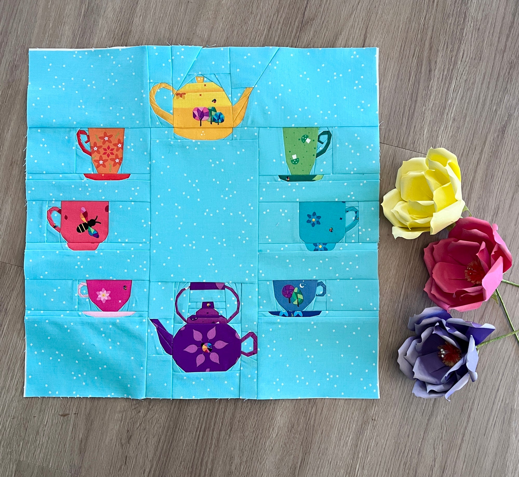 A collection of geometric teacups and teapots on a teal background. A playful FPP design perfect for tea lovers and colourful, whimsical quilts.