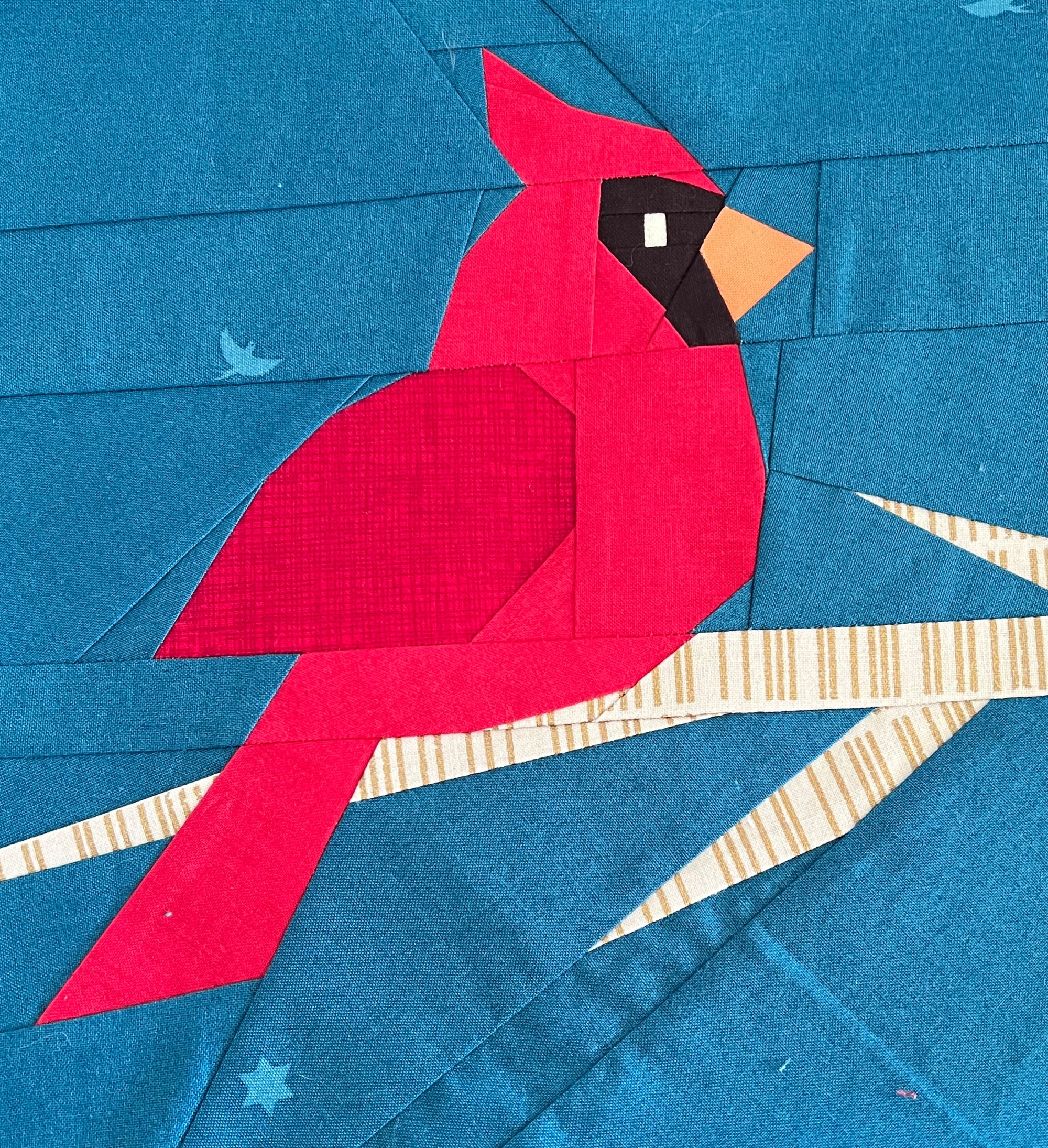 Close up of a red cardinal foundation paper pieced quilting pattern sewn on a blue background with branch details