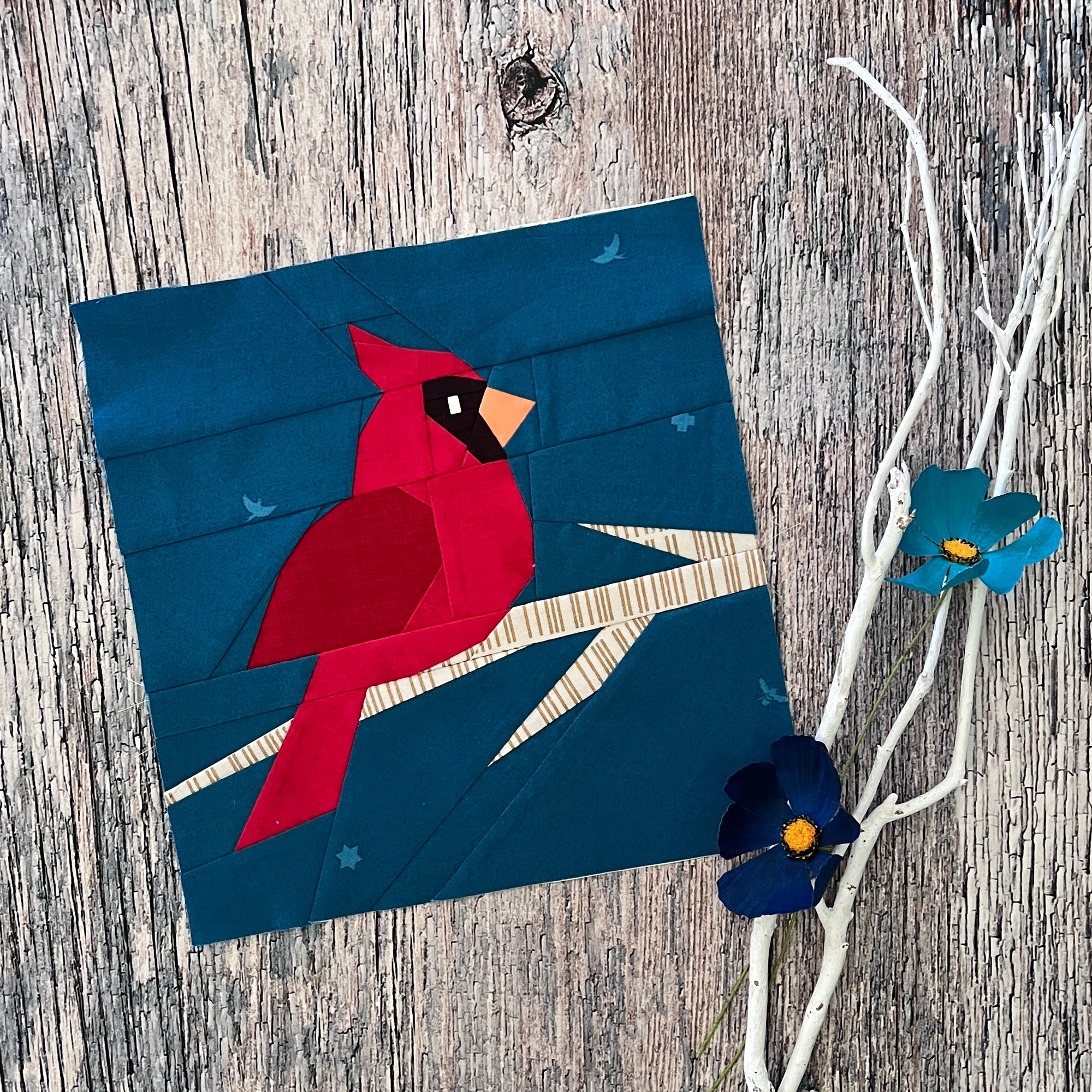 Finished winter cardinal foundation paper pieced quilting pattern block photographed on a rustic timber background